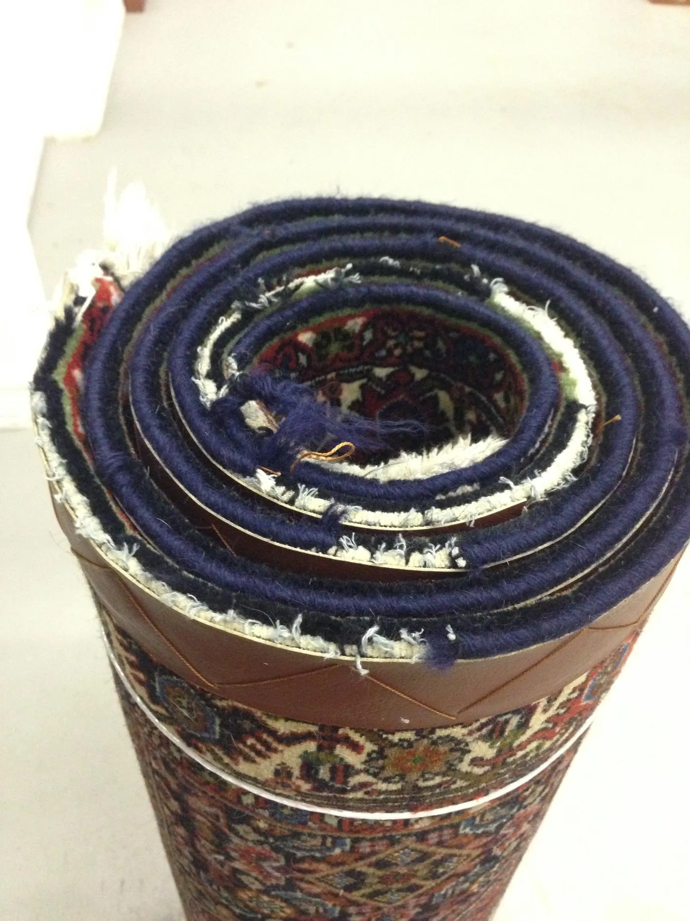 A rolled oriental rug showing a worn edge flagged for repair